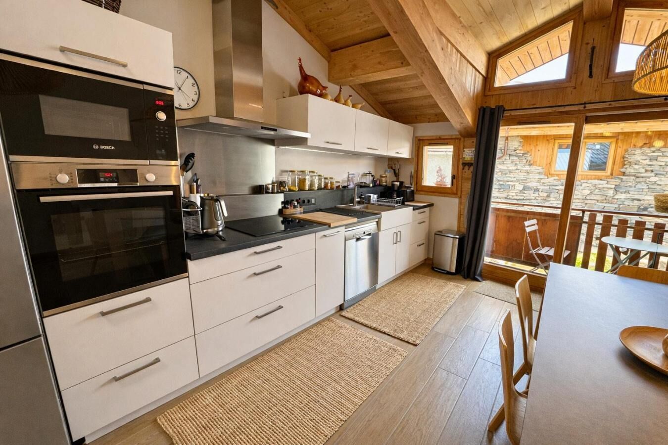 A modern kitchen with Bosch appliances, a stone wall outside, and a dining area with a view.