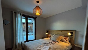 Une chambre à coucher avec un grand lit, deux lampes de chevet, une fenêtre avec des rideaux et un luminaire suspendu.