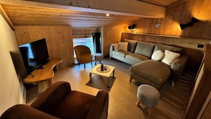 Un salon chaleureux avec des murs et un plafond en bois, un ensemble de canapés, un téléviseur et une table basse.
