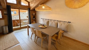 Un intérieur en bois avec une table, des chaises, un luminaire suspendu et une vue à travers une porte vitrée.