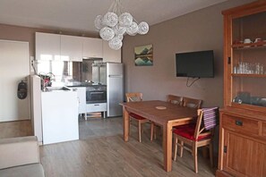 A modern kitchen with white cabinets, a dining table with chairs, a wooden cabinet with glassware, and a flat-screen TV mounted on the wall. - Ski-in/ski-out & foot of the slopes, 6th floor, view mountain, balcony, tv, 60m², Les Orres (Les Orres)