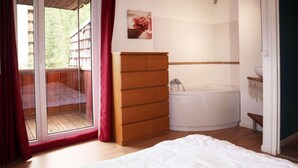 A bedroom with a bed, a wooden dresser, a bathtub, and a sliding glass door leading to a balcony. - Ski-in/ski-out & foot of the slopes, 6th floor, view mountain, balcony, tv, 60m², Les Orres (Les Orres)