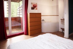 Ein Schlafzimmer mit Bett, einem Holzschrank, einer Badewanne und einer Glastür, die auf einen Balkon führt.