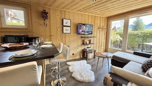 Et træpanelt interiør med et spisebord, en sofa og et fjernsyn.