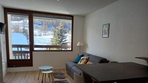 Een moderne woonkamer met een bank, een eettafel en zicht op een besneeerd landschap door grote ramen.