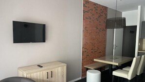 Een moderne hotelkamer met een flatscreen televisie, een houten kast, een eettafel en een accentmuur van baksteen.
