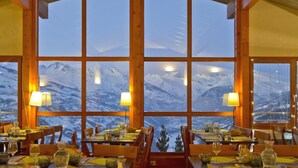 Ein Restaurant mit mehreren Tischen und Stühlen, großen Fenstern mit Bergblick und warmer Innenraumbeleuchtung.