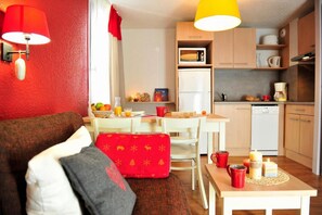 Un espacio habitable compacto con comedor, kitchenette y una decoración en rojo y blanco.