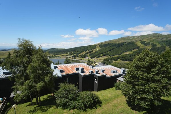 Un edificio moderno de techo plano, rodeado de exuberante vegetación y un lago al fondo.