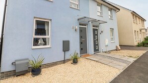 A two-story residential building with a light blue exterior, a dark grey door, and a small garden area with gravel and potted plants. - Tŷ Glas (Bridgend)