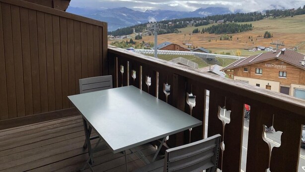 En balkon med et bord og stole, med udsigt over en by med bjerge i baggrunden.