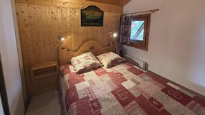 Et rum med træpaneler, en seng, et natbord, et vindue med gardiner og et skilt på væggen.