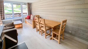 A modern living room with a wooden dining table and chairs, a sofa, and a window with curtains. - 1st floor, balcony, tv, ski locker, 58m², Tignes (Tignes)