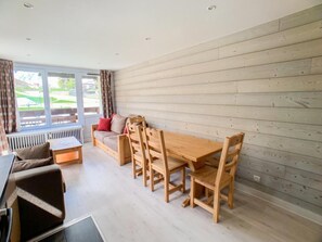 Una sala de estar moderna con una mesa y sillas de madera, un sofá y una ventana con cortinas.