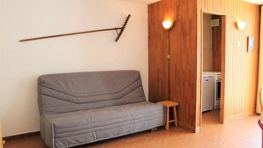 A room with a grey sofa, wooden panel walls, a small wooden stool, and a washing machine in the background. - Resort center, 1st floor, balcony, tv, 30m², Vars (Vars)