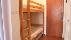 A bunk bed with a wooden frame and a mattress in a room with a wooden door and a light switch on the wall. - Resort center, 1st floor, balcony, tv, 30m², Vars (Vars)