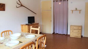 A dining area with a wooden table and chairs, a television on a wooden cabinet, a door with a curtain, and a small wooden dresser. - Resort center, 1st floor, balcony, tv, 30m², Vars (Vars)