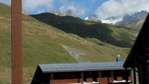 Un chalet de montagne avec un toit en métal, des murs en bois et une vue sur des sommets enneigés.