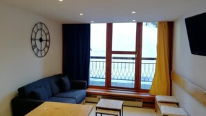 Ein Zimmer mit einem blauen Sofa, einem kleinen Tisch, einer Wanduhr und Meerblick durch ein großes Fenster.