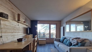 A modern living room with a wooden dining table, a sofa, and a large window providing a view of the outdoors. - 100m from ski slopes, 1st floor, swimming pool, balcony, tv, 31m², Les Arcs (Les Arcs)