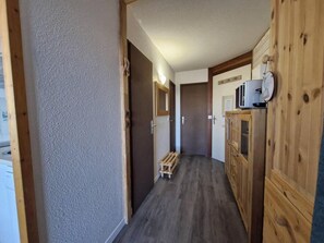 A narrow hallway with wooden cabinets, a small wooden bench, and a microwave on a cabinet.