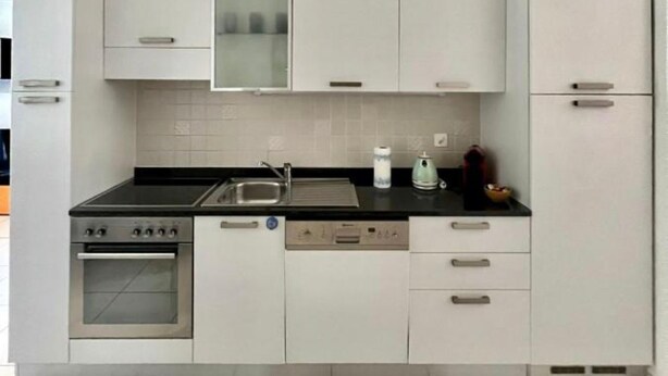 A modern kitchen with white cabinets, a black countertop, a built-in oven, and a dishwasher. - 2 bedroom apartment in lower morbio (Morbio Inferiore)