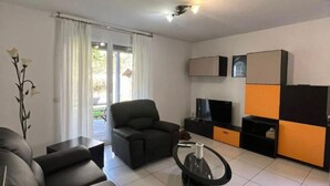 A modern living room with a sofa, armchair, and coffee table. There is a TV and a cabinet with orange and black accents. - 2 bedroom apartment in lower morbio (Morbio Inferiore)
