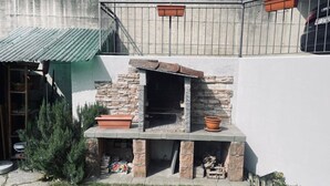 A stone-built outdoor kitchen with a chimney, surrounded by a small garden and a metal fence. - 2 bedroom apartment in lower morbio (Morbio Inferiore)