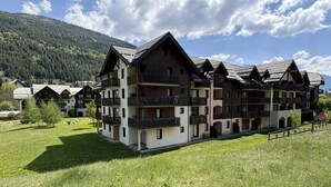A multi-story building with balconies, surrounded by a grassy field and mountains in the background. - 100m from resort center, Ground floor, terrace, tv, ski locker, 42m², Serre Chevalier (La Salle-les-Alpes)