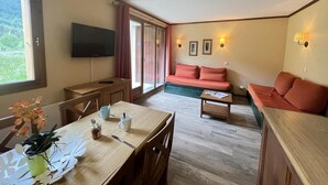 A cozy room with a wooden dining table, a sofa, and a television. - 100m from resort center, Ground floor, terrace, tv, ski locker, 42m², Serre Chevalier (La Salle-les-Alpes)