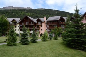 Een meerlaags hotel met balkons, omringd door een verzorgd gazon en bomen, gelegen tegen een bergachtige achtergrond.