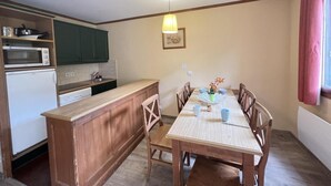 A compact kitchen with a dining area, featuring a wooden table, chairs, a small island, and basic appliances. - 100m from resort center, Ground floor, terrace, tv, ski locker, 42m², Serre Chevalier (La Salle-les-Alpes)