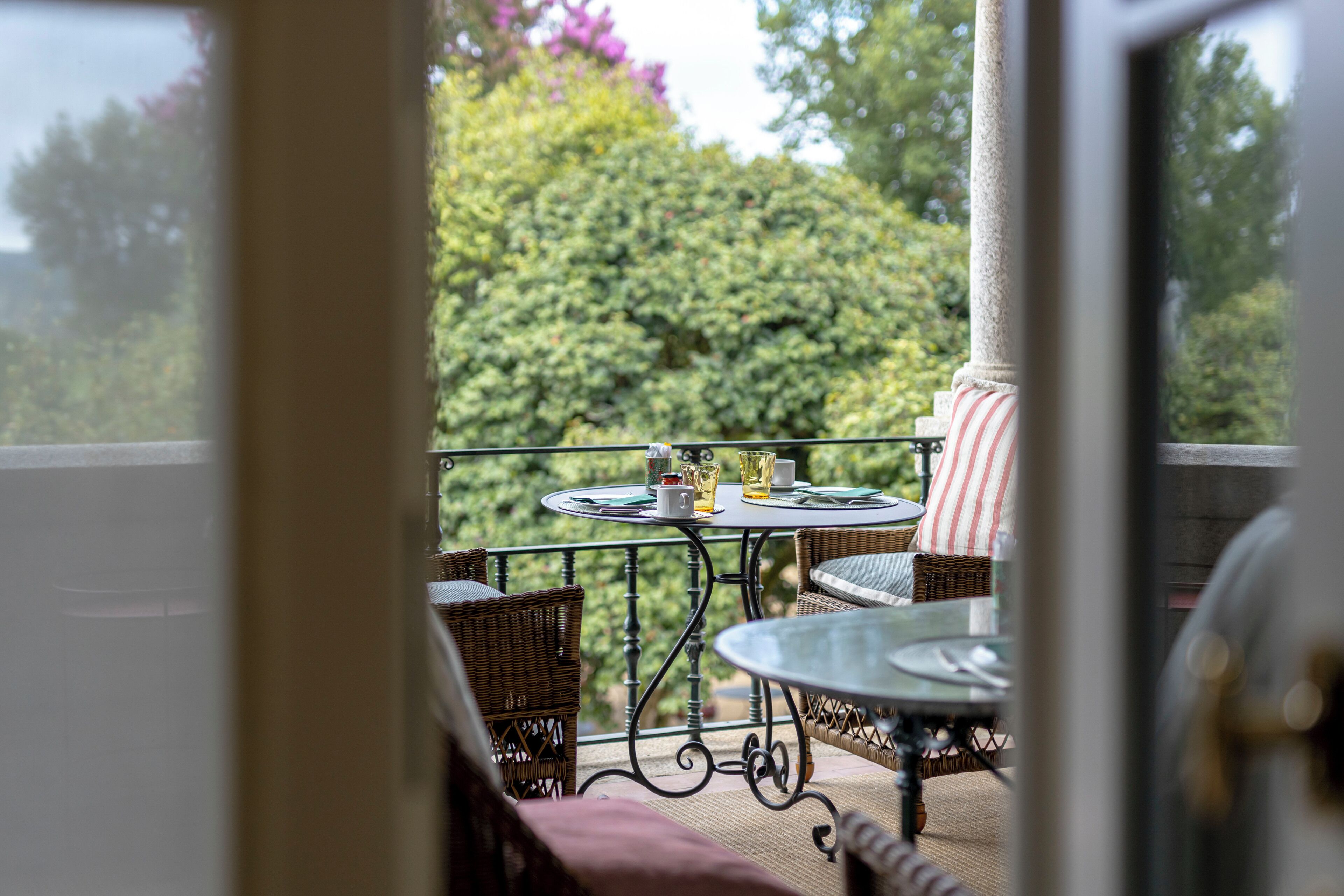 Varanda com mobiliário de vime e uma mesa, com vista para um jardim exuberante.