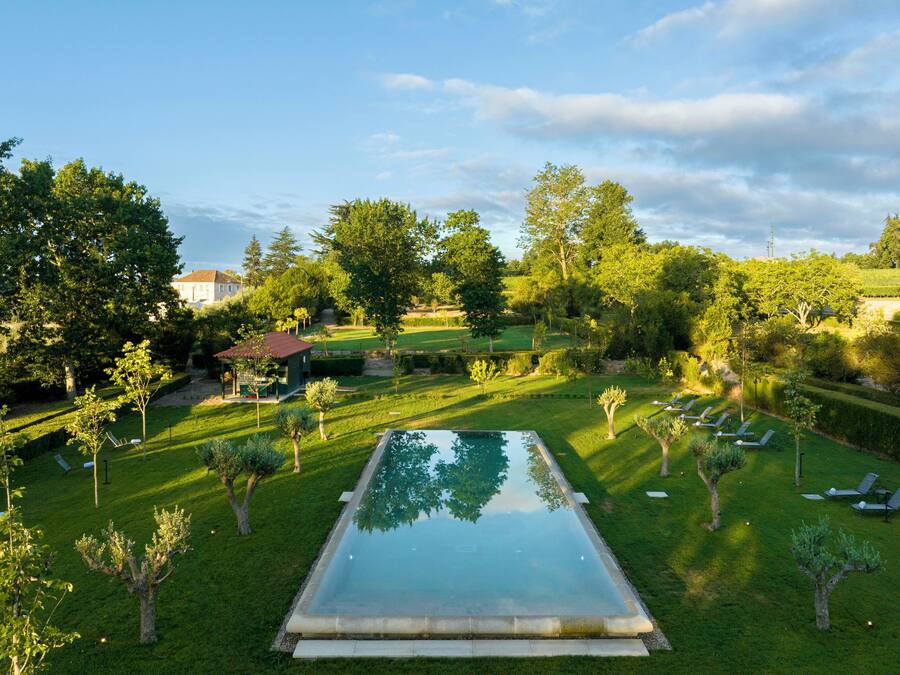 Una piscina rectangular rodeada de césped cuidado, con varias tumbonas y un pabellón al fondo.