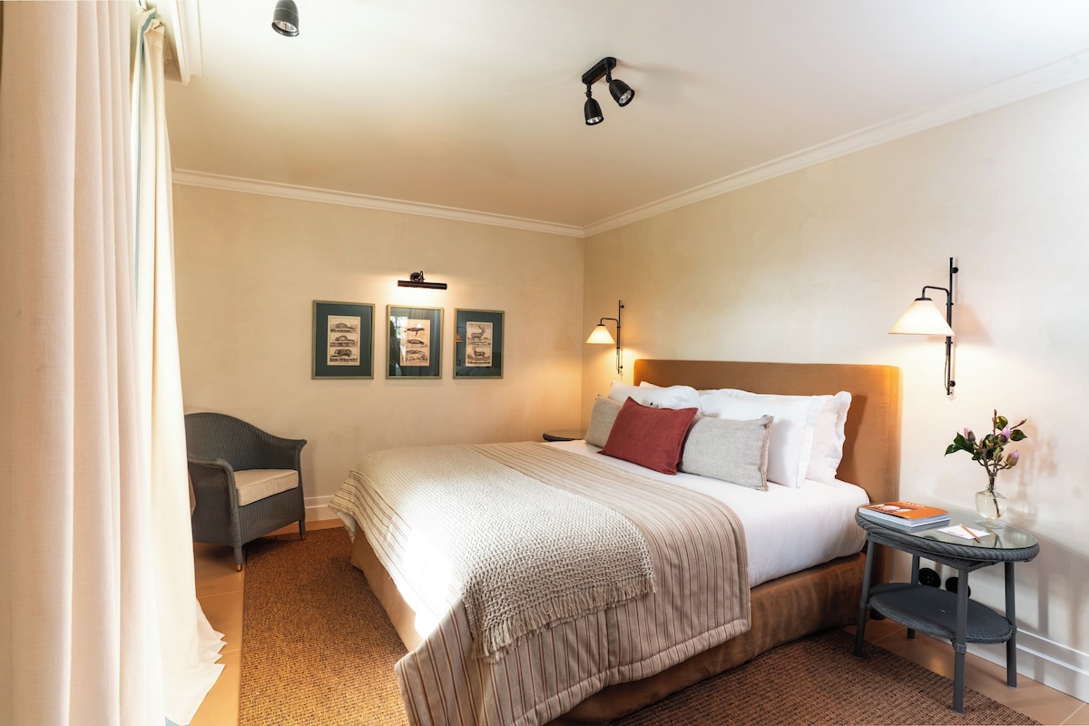 A hotel room with a bed, bedside table, lamp, and wall-mounted artwork.