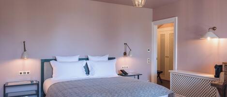 Un dormitorio ordenado con una cama, mesitas de noche, una lámpara y una puerta que da a otra habitación.
