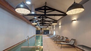 A modern indoor pool area with a long bench seating along one side, multiple pendant lights, and a visible pool with a clear water surface. - Valverde Santar Hotel & Spa – Relais & Châteaux (Nelas)