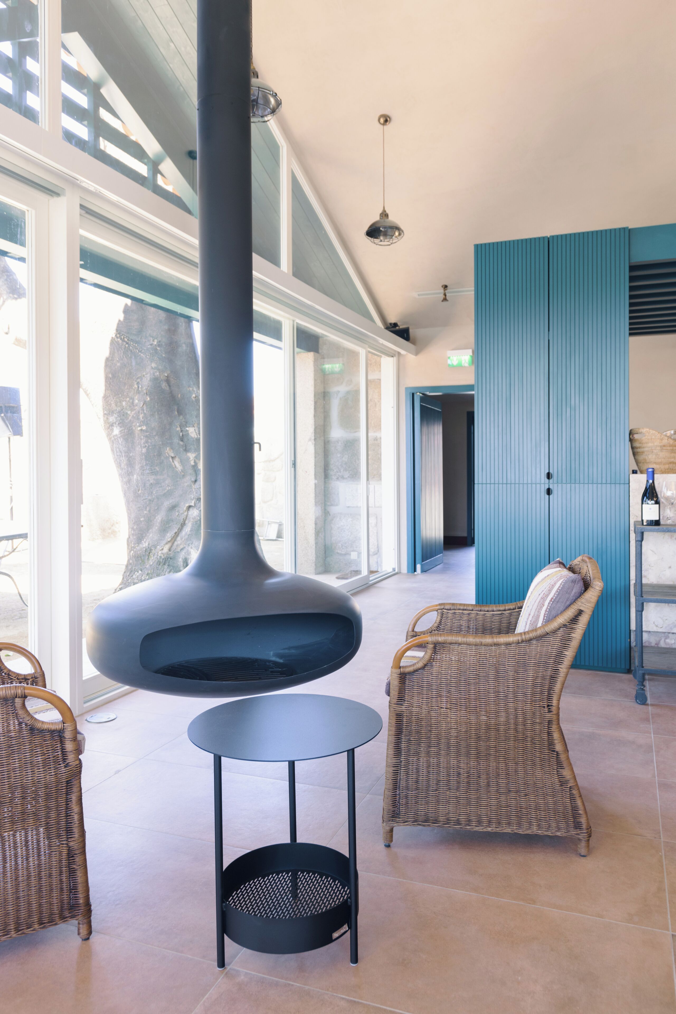 A spacious indoor area with a large, modern fireplace, wicker furniture, and a view through large glass doors.