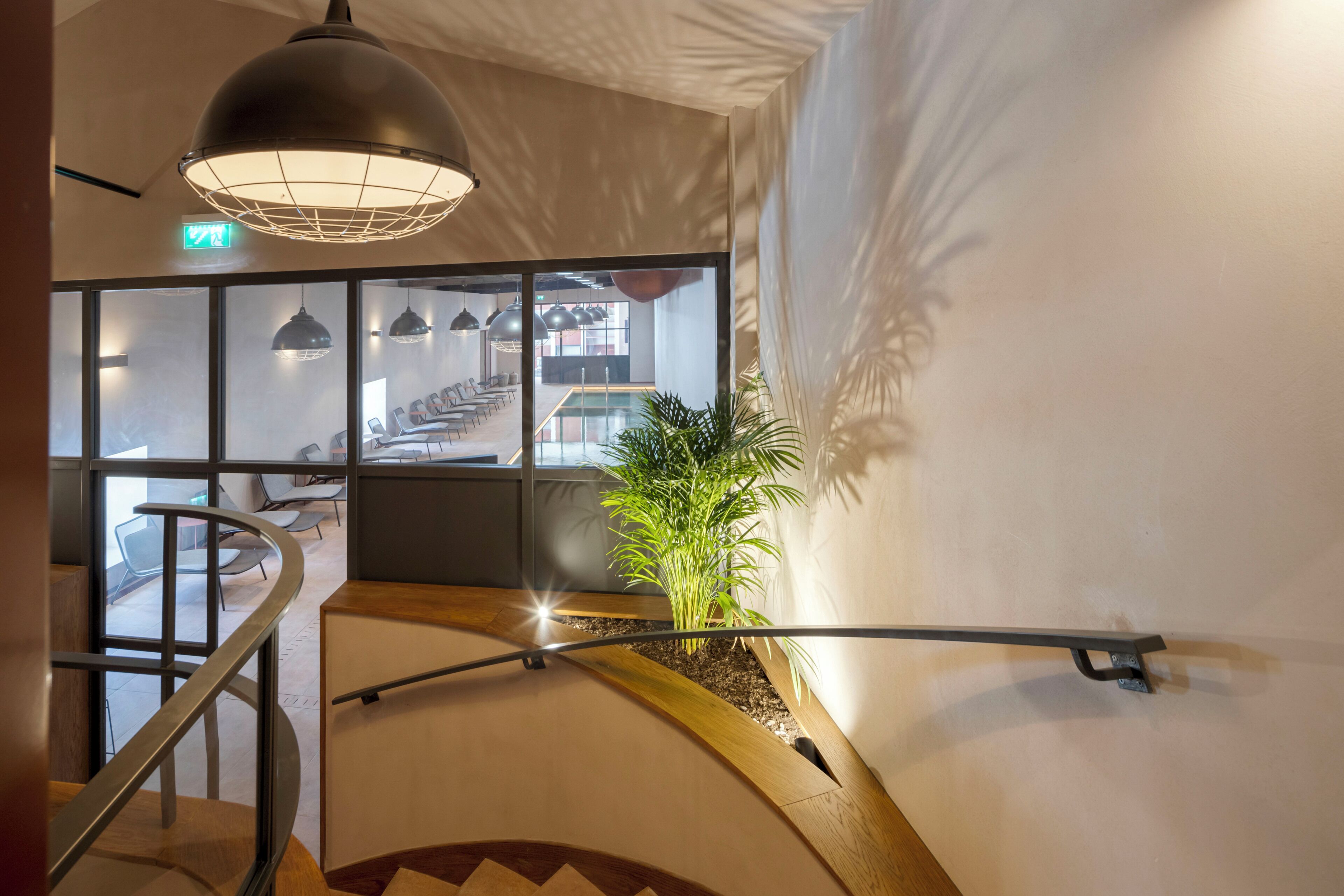 Un interior moderno con una escalera curva, una lámpara colgante grande y vistas a una zona de estar a través de un muro de cristal.