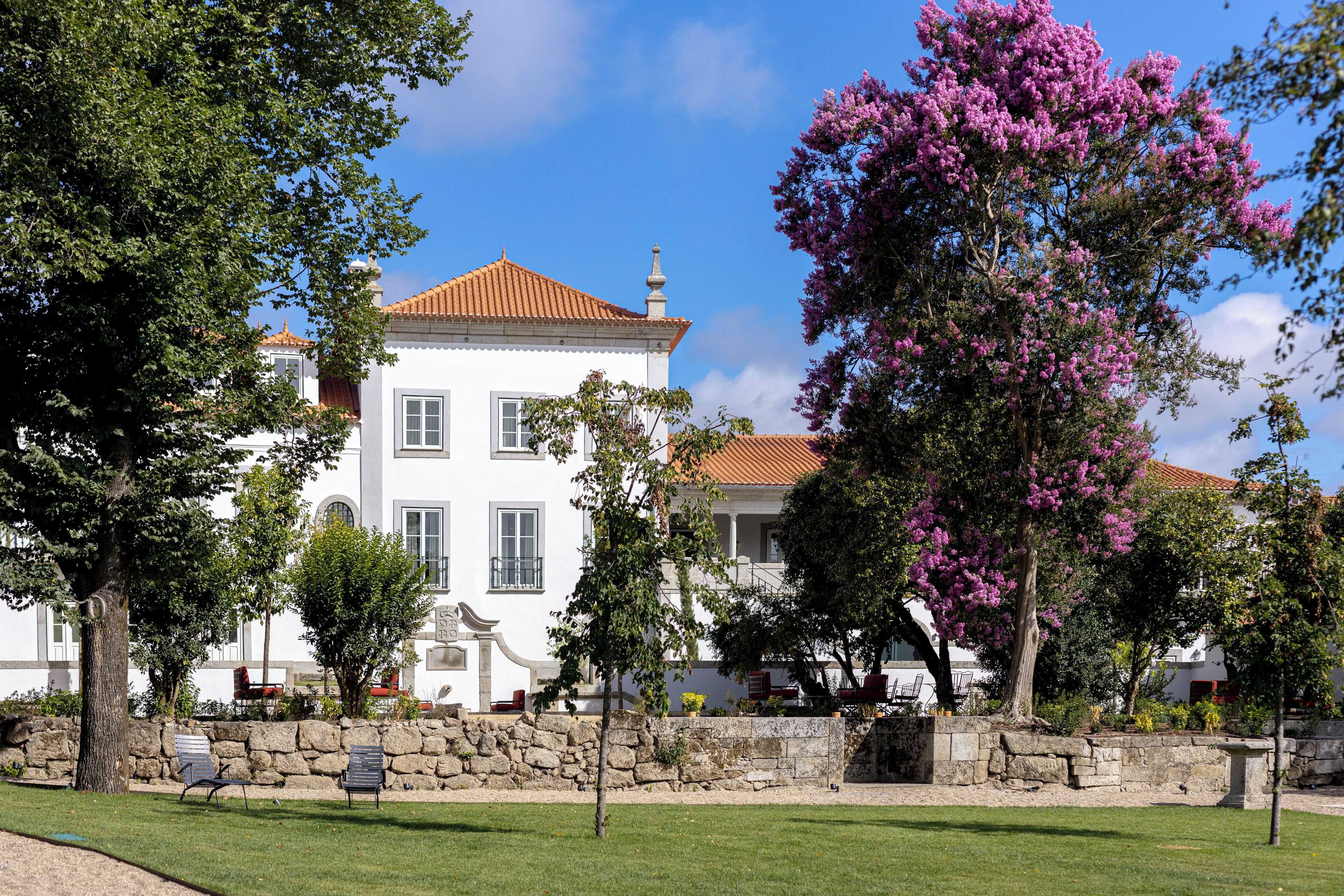 A white building with a red roof, surrounded by a stone wall and green lawn.