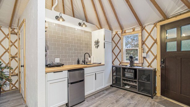 A compact kitchen with white cabinets, a stainless steel refrigerator, and a wooden countertop.