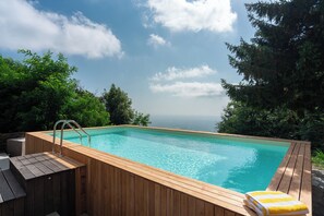 A wooden infinity pool with a wooden deck, surrounded by lush greenery and a clear sky. - Casa Sul Serra (Calci)