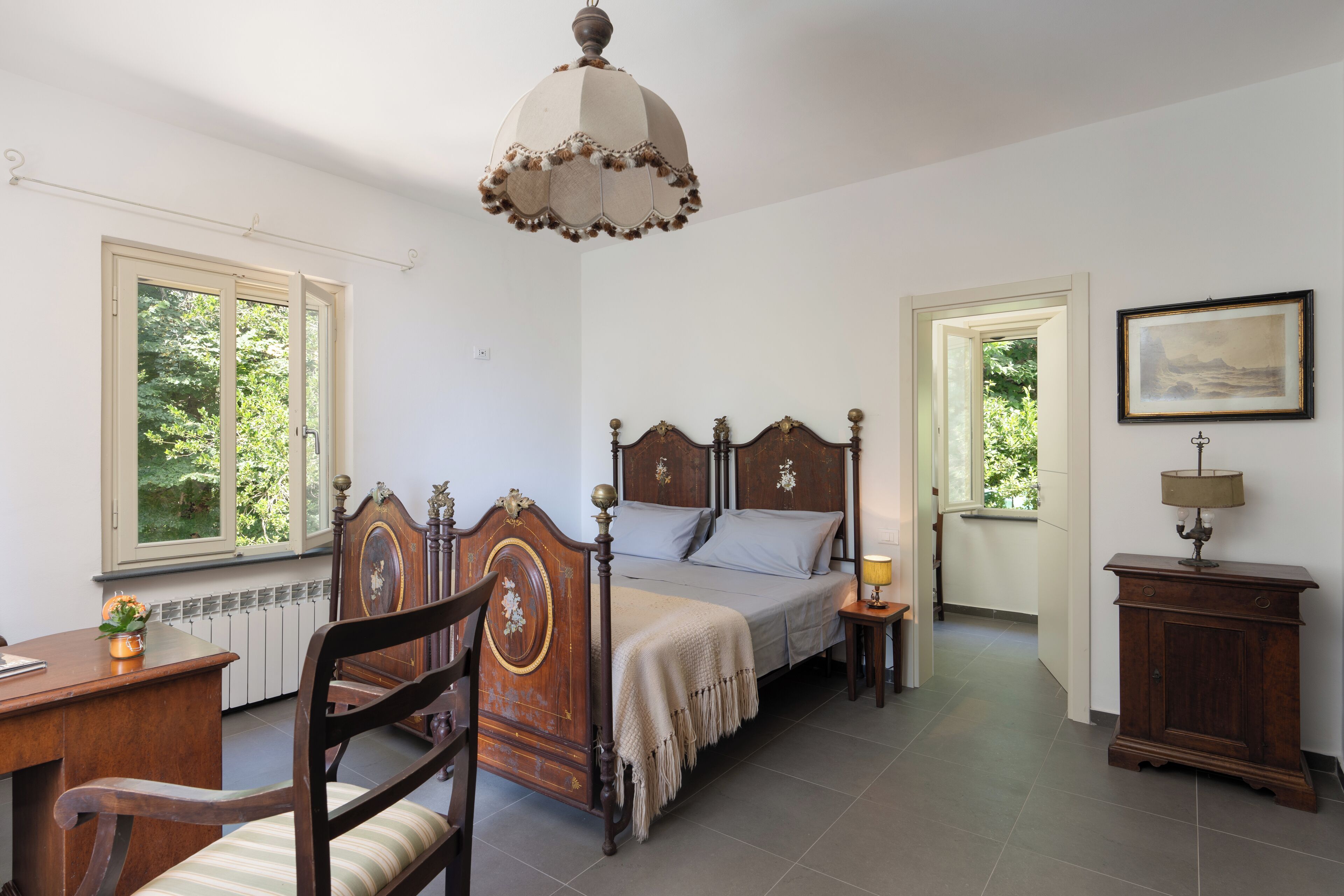 Una camera da letto con un letto in legno, una scrivania, una sedia, un comodino con una lampada e un quadro incorniciato appeso al muro.