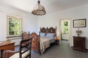 A bedroom with a wooden bed, a desk, a chair, a bedside table with a lamp, and a framed picture on the wall. - Casa Sul Serra (Calci)
