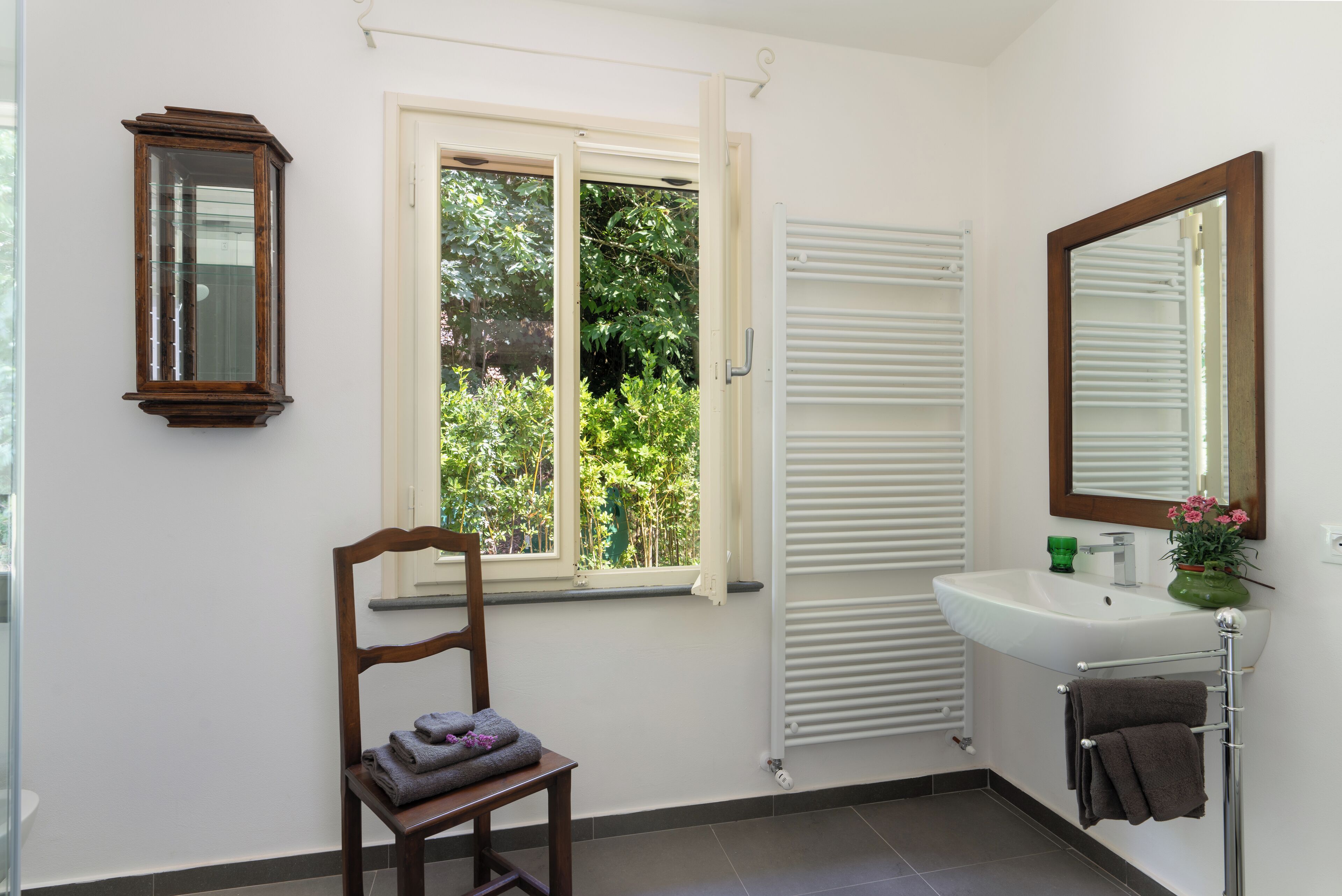 A bathroom with a window, a wooden chair, a sink, and a mirror.