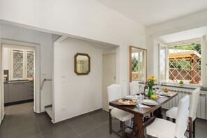 A dining area with a table set for four, a mirror on the wall, and a window with a view of greenery outside. - Casa Sul Serra (Calci)