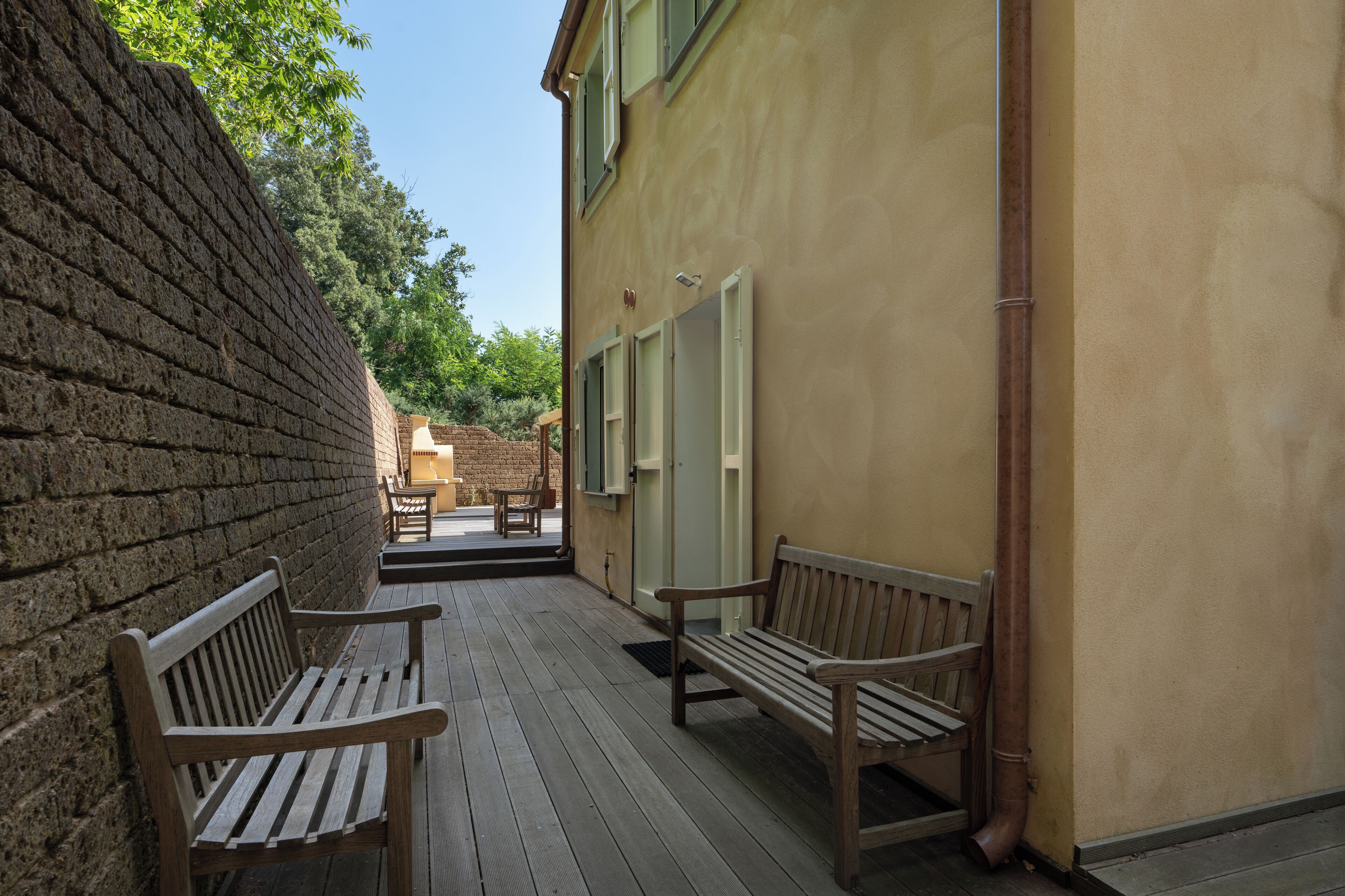 Una terraza de madera con bancos, un muro de ladrillo y un edificio amarillo con ventanas.