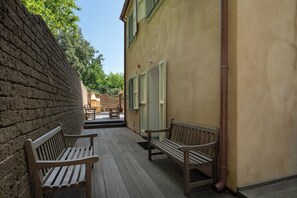 A wooden deck with benches, a brick wall, and a yellow building with windows. - Casa Sul Serra (Calci)