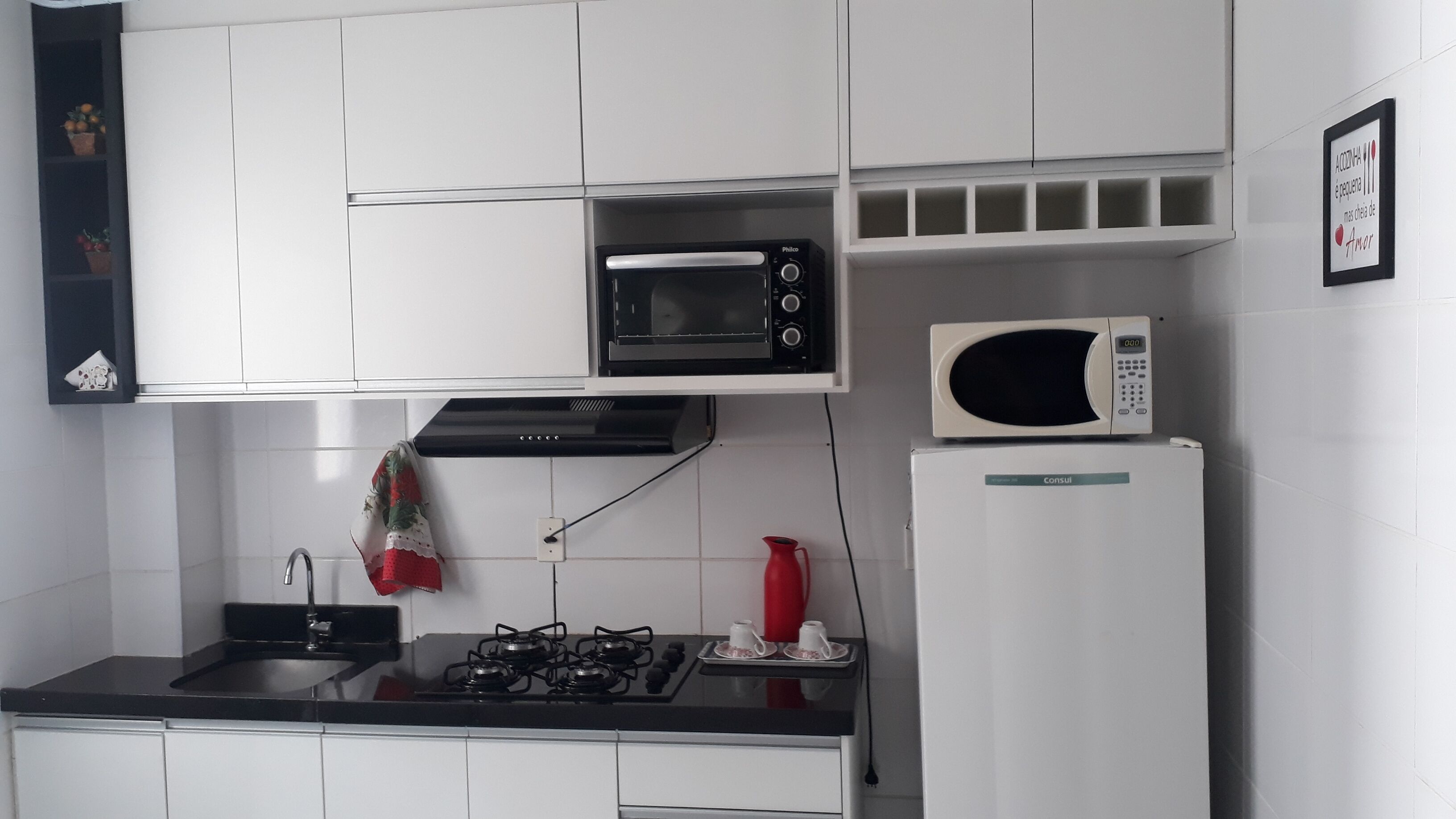 Eine Küche mit weißen Schränken, einem schwarzen Gaskochfeld, einer schwarzen Mikrowelle und einem weißen Kühlschrank.