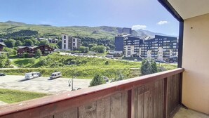 Un balcon donnant sur un parking, des immeubles et des collines verdoyantes.